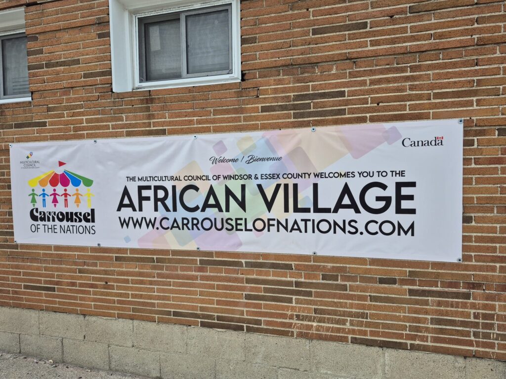 The African Village banner on the brick wall of the venue, welcoming visitors on behalf of the Multicultural Council of Windsor and Essex County.