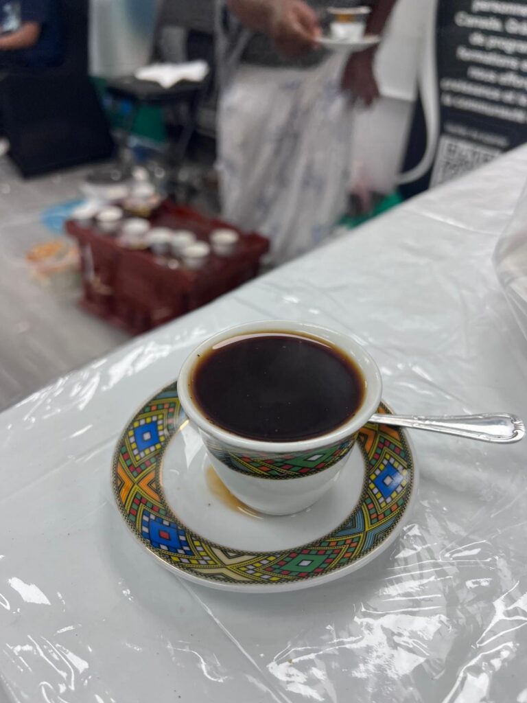 A close view of a full coffee cup and patterned saucer on the covered serving table at the BCCEEP Centre, with a cup being carried away in the background
