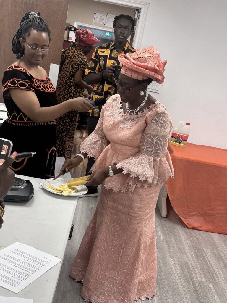A guest in a pale embroidered dress and head tie being served from the food table at BCCEEP Hall.