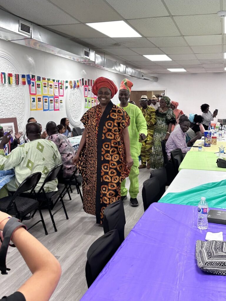 A guest in a patterned robe and red cap walking past tables dressed with purple and green cloths at BCCEEP Hall.