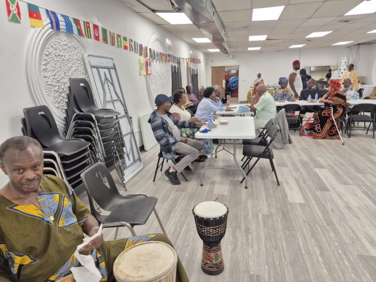 Drums set out on the floor at the BCCEEP Centre, with flag bunting overhead and people seated at tables