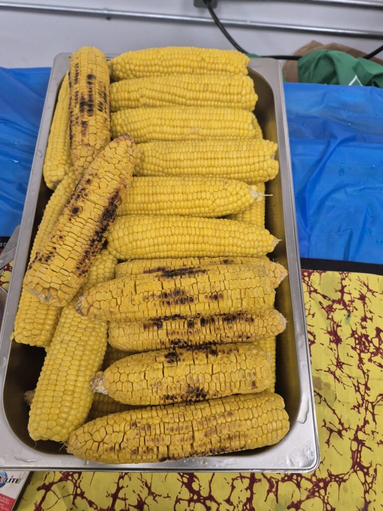 A metal tray stacked with charred grilled corn cobs on a patterned cloth at BCCEEP Hall.