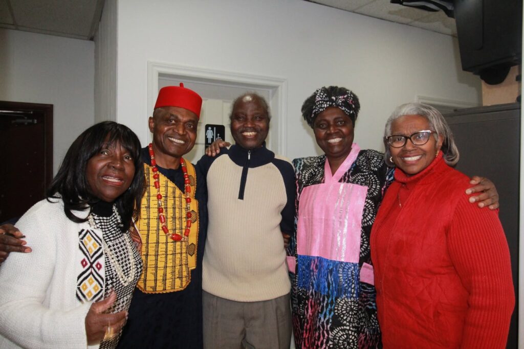 Five guests standing arm in arm for a photograph, one in a red cap and yellow patterned top.