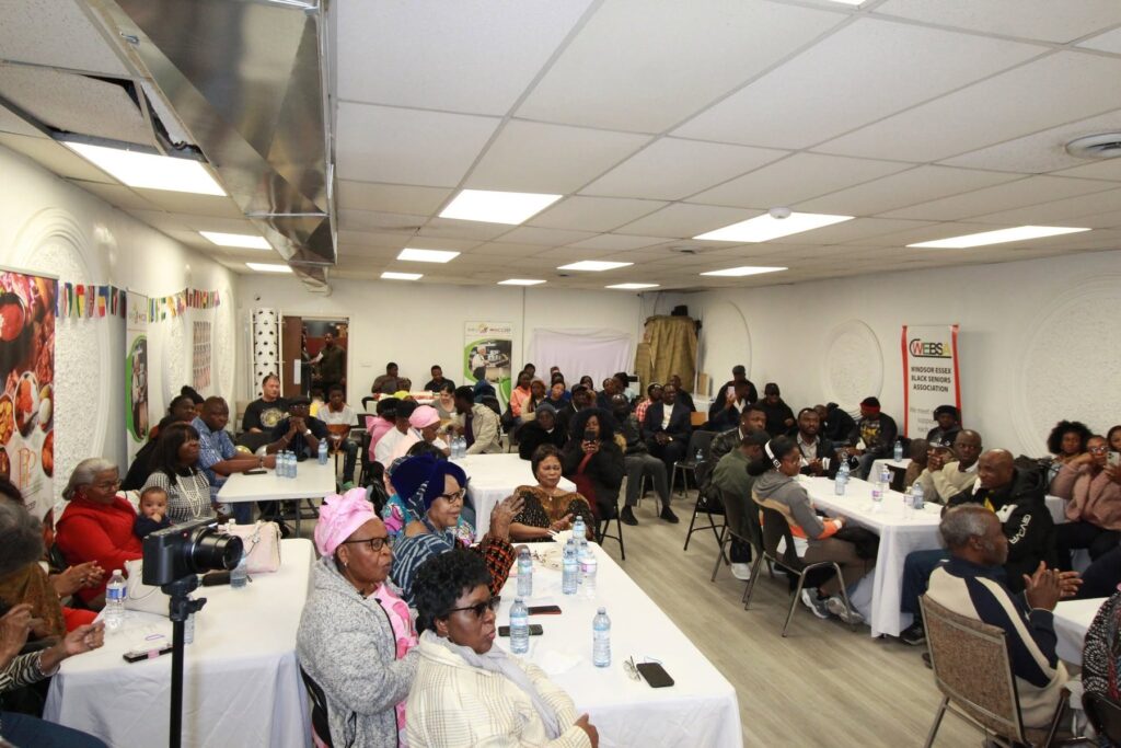 A wide view of the room filled with seated guests at long tables, exposed ductwork across the ceiling.