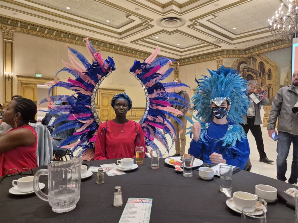 Two performers in blue feathered headdresses seated at a banquet table at the Ciociaro Club.