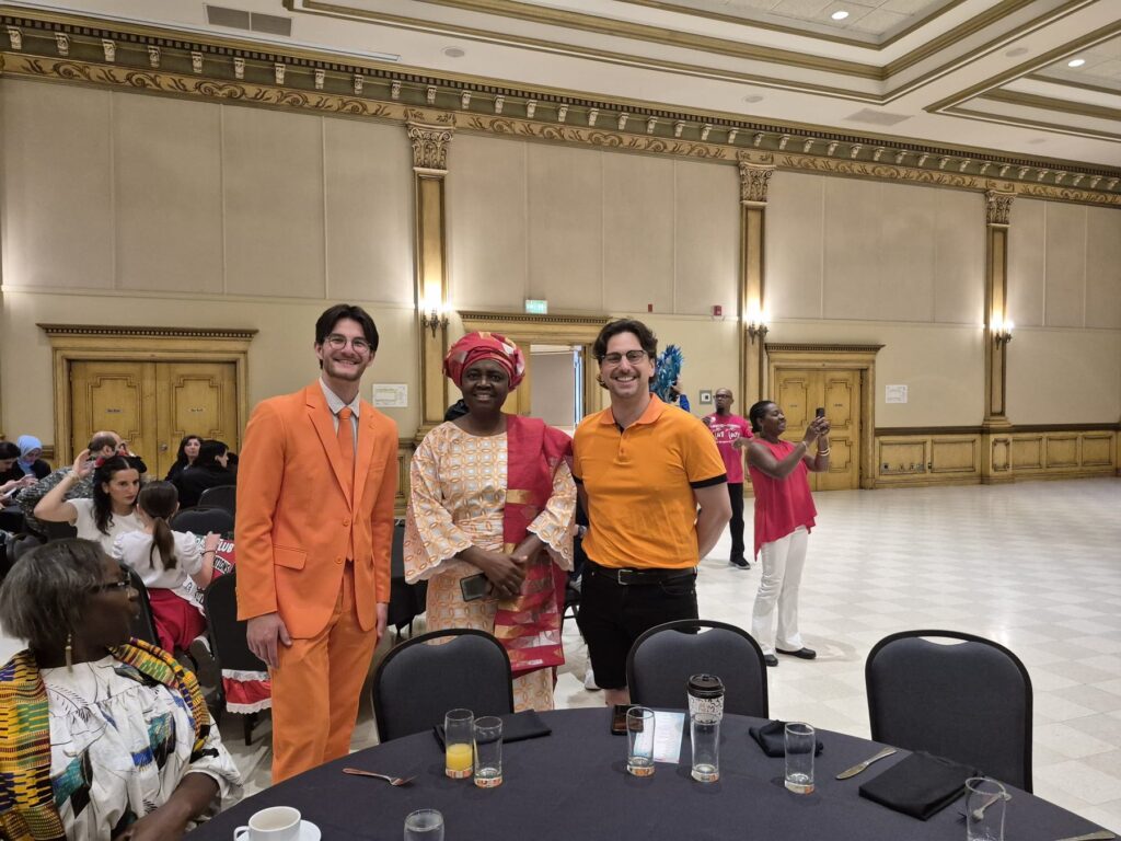 Two guests in matching orange suits standing at the Ciociaro Club, another guest in a red head tie beside them.
