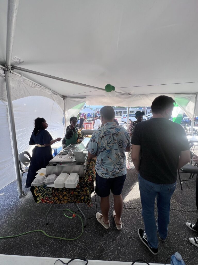 Guests serving themselves from covered trays on a patterned tablecloth at the Nigerian Village food table