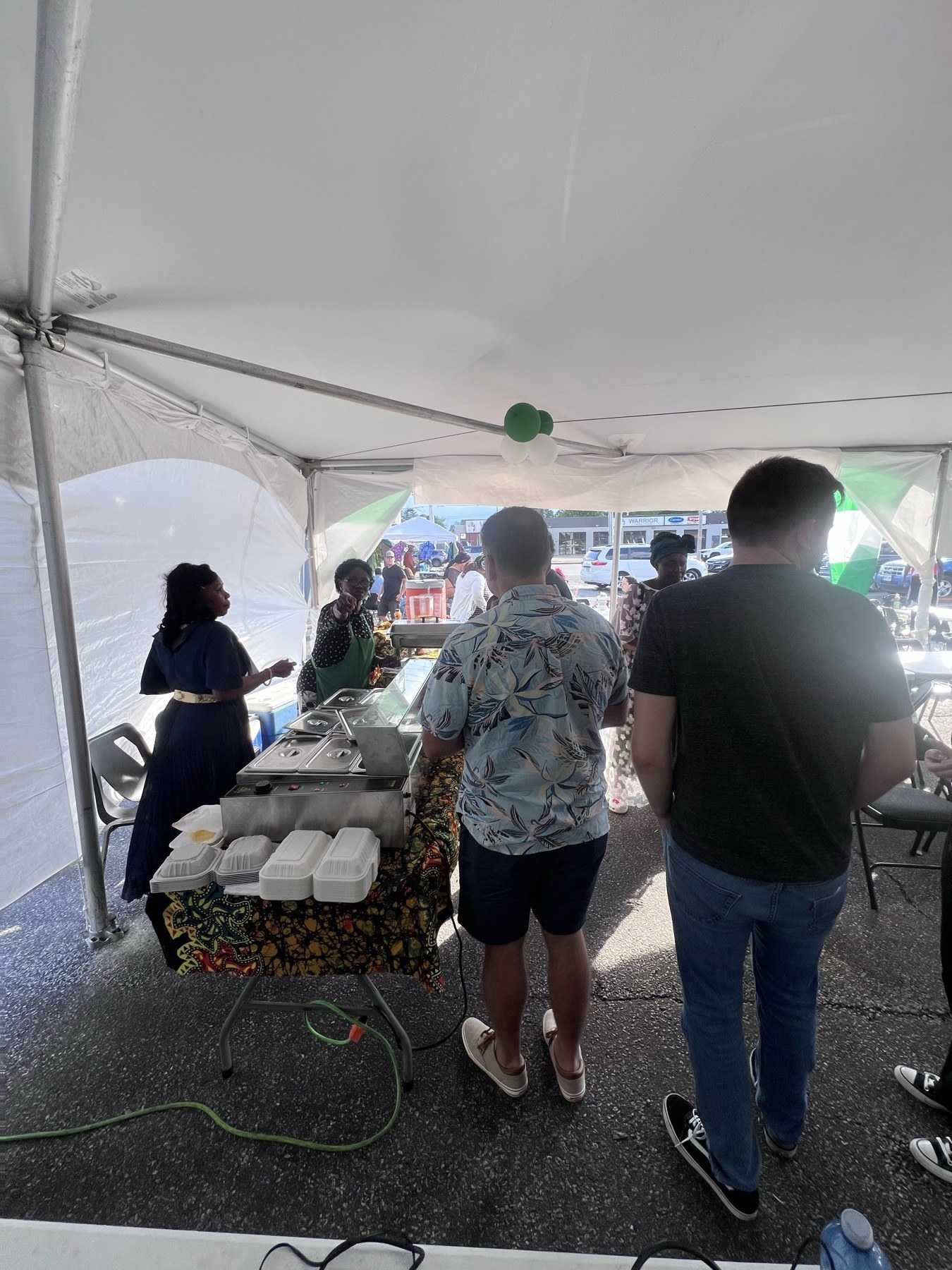 Guests serving themselves from covered trays on a patterned tablecloth at the Nigerian Village food table