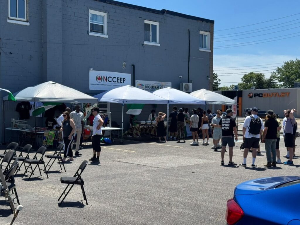 Market stalls under white canopies in the parking lot at the Nigerian Village on Walker Road in Windsor, with visitors queuing at the food tent