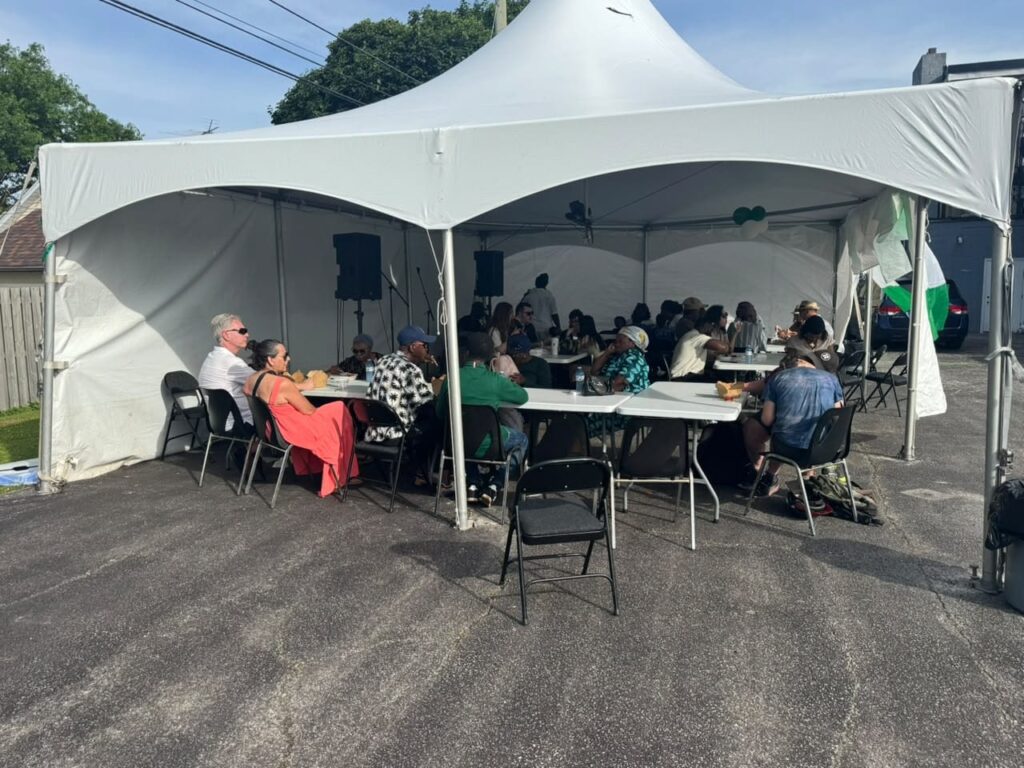 Guests seated on folding chairs at long tables inside a white marquee at the Nigerian Village on Walker Road in Windsor