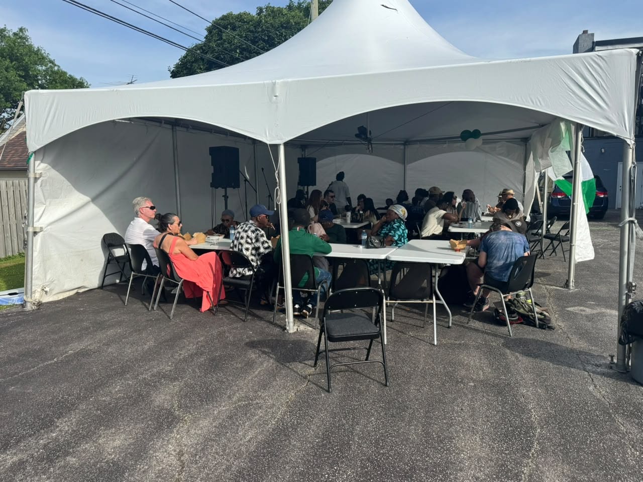 Guests seated on folding chairs at long tables inside a white marquee at the Nigerian Village on Walker Road in Windsor