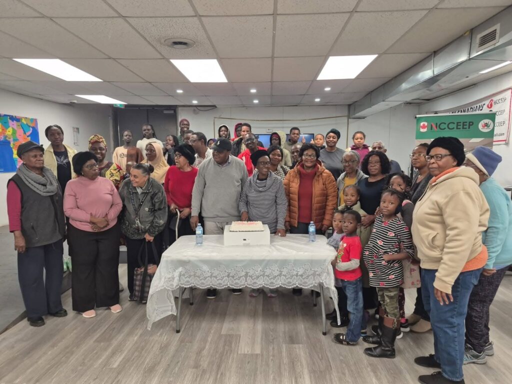 The whole group standing together behind a table set with a white cake at the November gathering.
