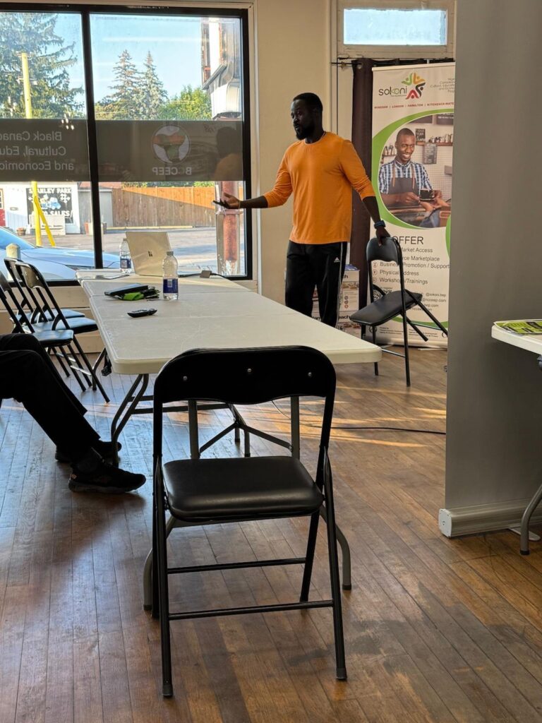 A facilitator in an orange shirt speaking to the group from beside a roll-up banner.